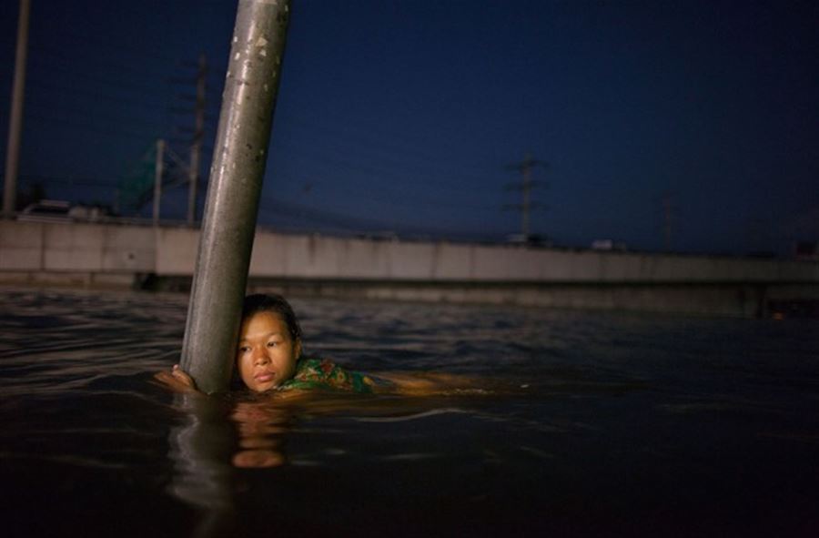 A woman hangs onto a street sign in chest deep water along the flooded streets in Rangsit on the outskirts of Bangkok, on October 24, 2011. (Paula Bronstein/Getty Images)